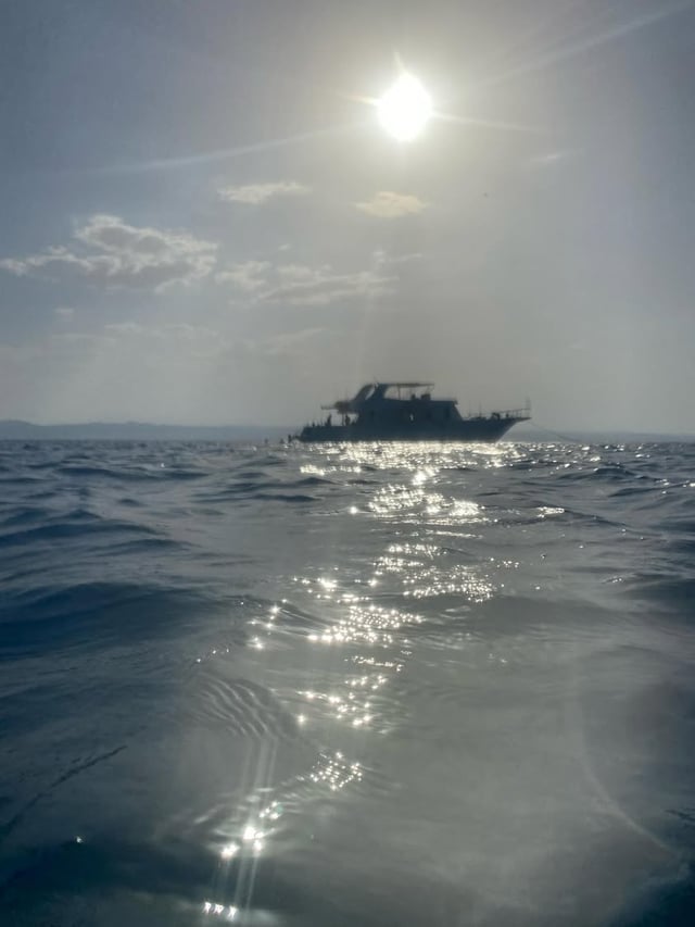 A boat silhouetted on the water beneath a bright sun, with sunlight scattered across the sea.