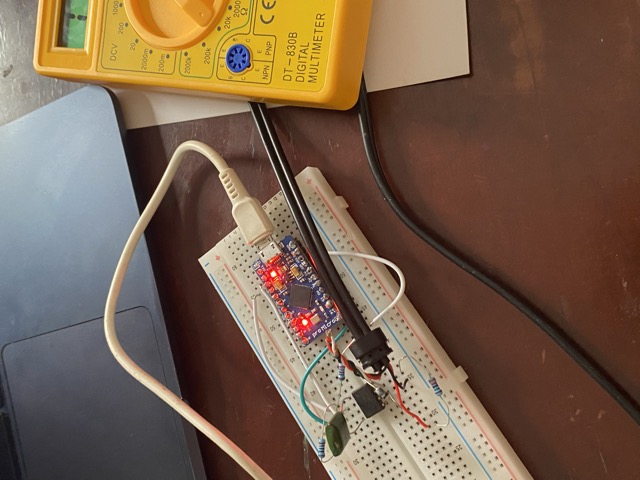 An Arduino Pro Micro on a breadboard, wired to a MIDI socket, beside a yellow multimeter and a laptop.