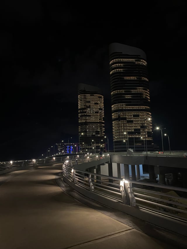 Two illuminated towers at night above a curved waterfront walkway.
